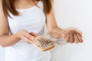 Woman holding a wooden hairbrush filled with loose strands while gathering more hair in her other hand.