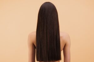 Back view of a woman with long, straight dark hair against a peach-colored background.