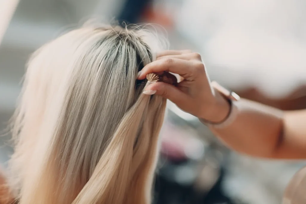 stylist placing individual hair extension strands into blonde hair during salon appointment