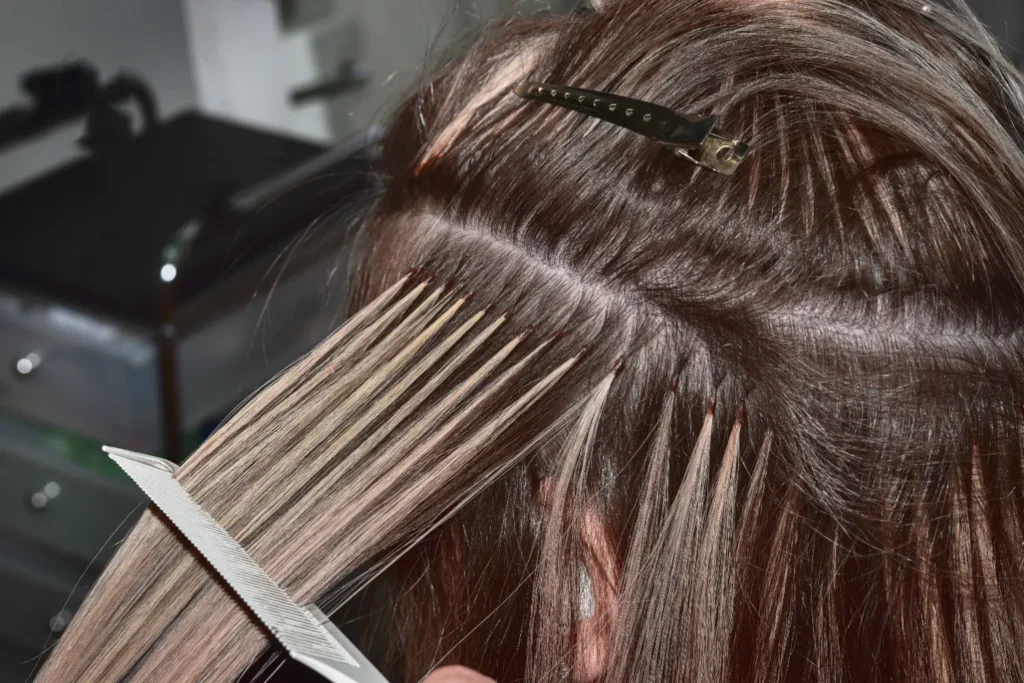 close-up of stylist installing hair extensions using bead or micro-link method at scalp