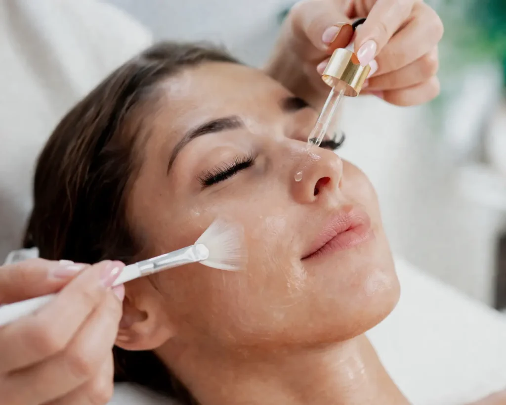 Close-up of serum being applied to a woman’s face with a dropper and brush