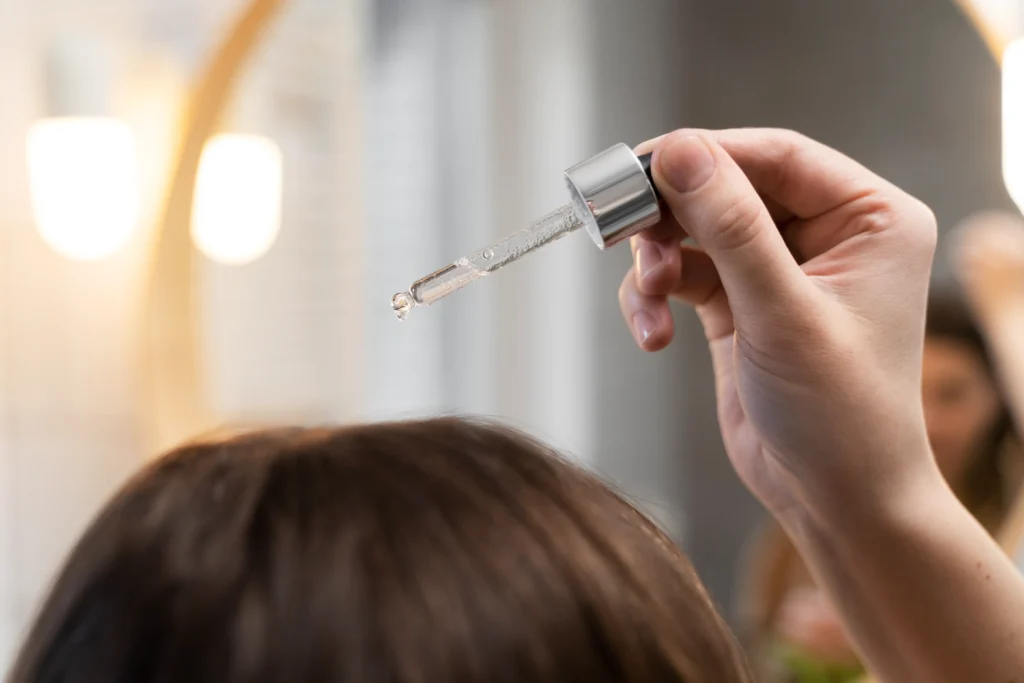 Hand holding dropper with clear serum above hair