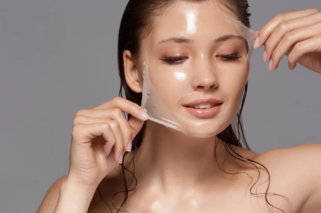 Person peeling a transparent facial mask from their face against a neutral background.