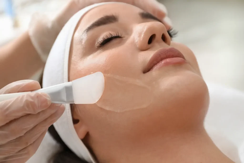 Practitioner applying a chemical peel solution to a person's cheek with a flat applicator.
